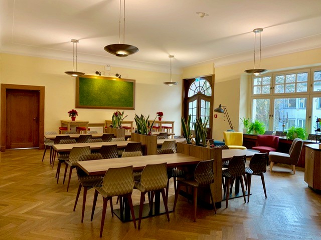 Ein Aufenthaltsraum mit Tischen, Stühlen und Parkettboden.