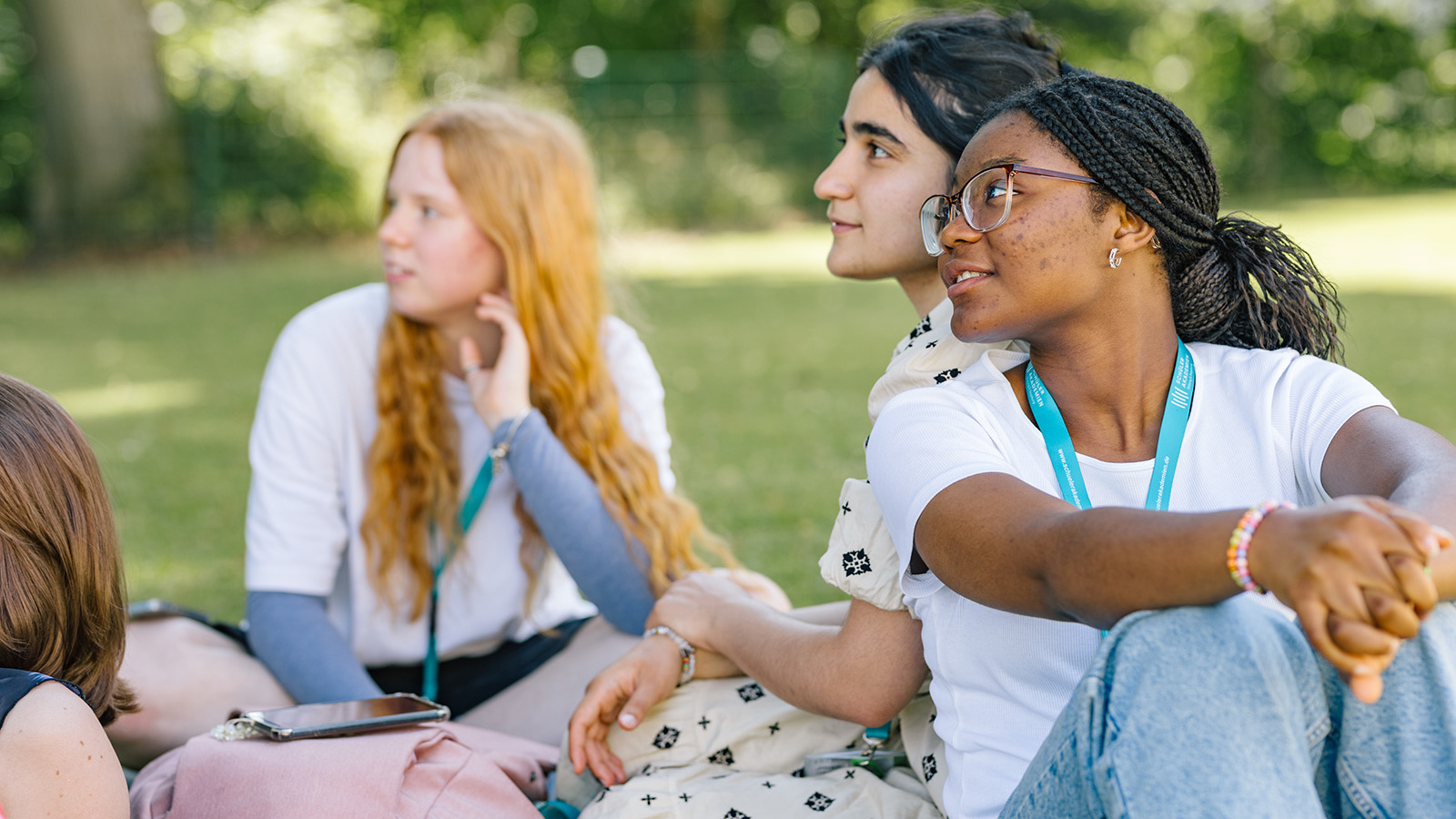Einige junge Personen sitzen auf einer Wiese und schauen nach links.