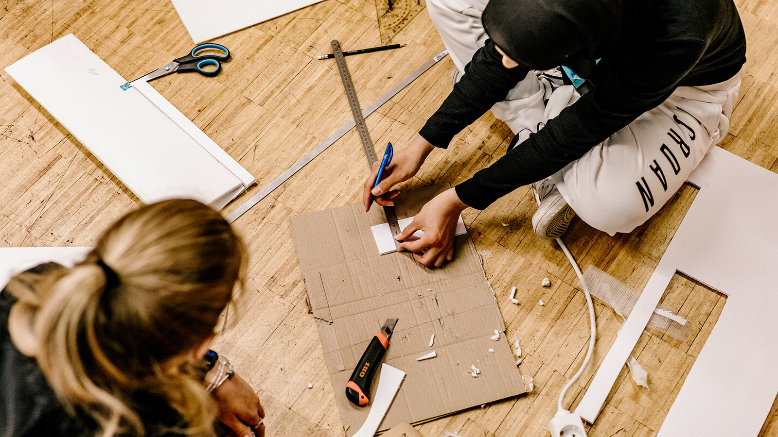 Von oben sind zwei Jugendliche zu sehen, die mit Cuttermessern Pappe und Holz bearbeiten.