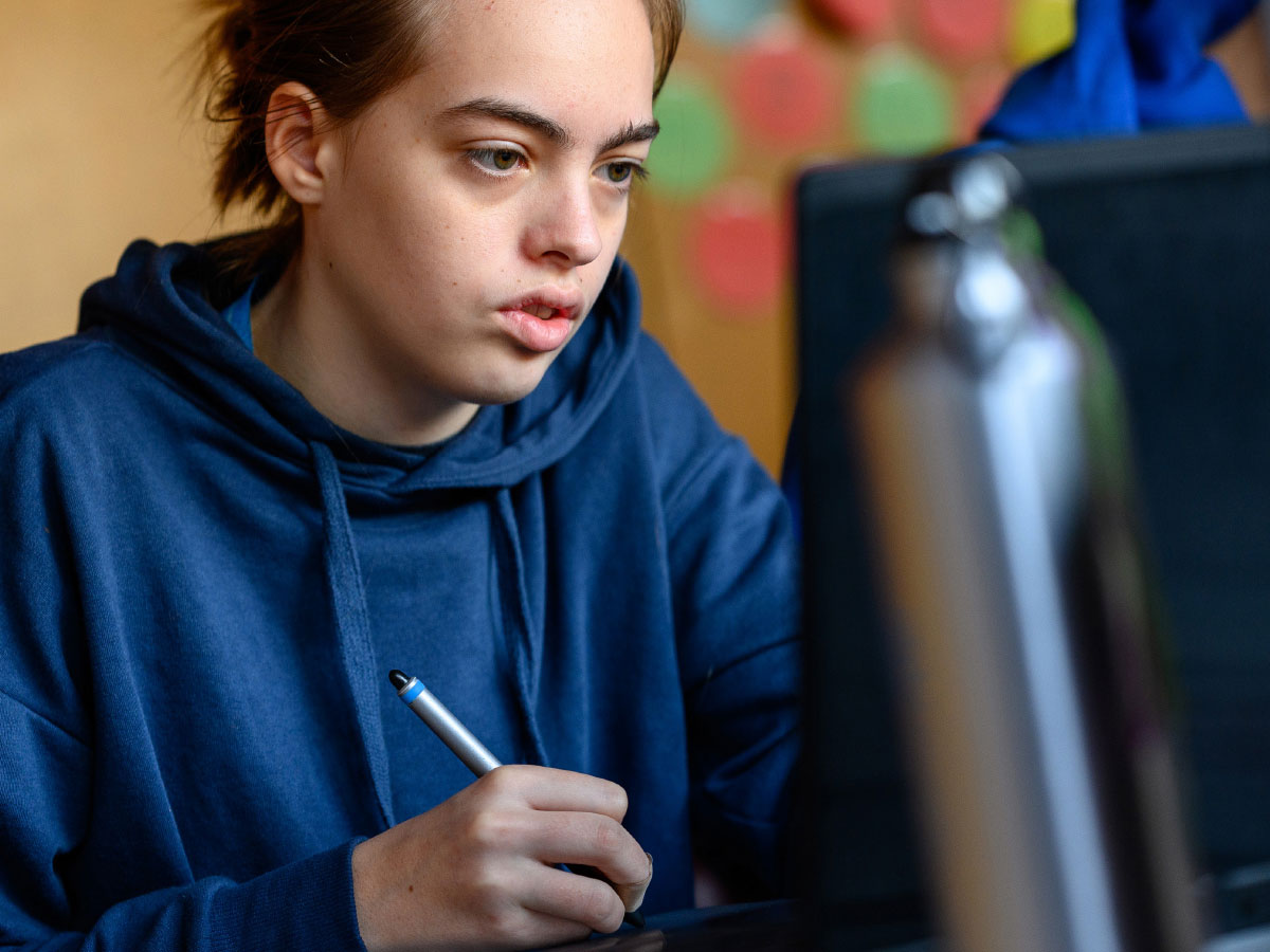 Ein Mädchen schaut konzentriert auf einen Computer und hält einen Stift in der Hand.