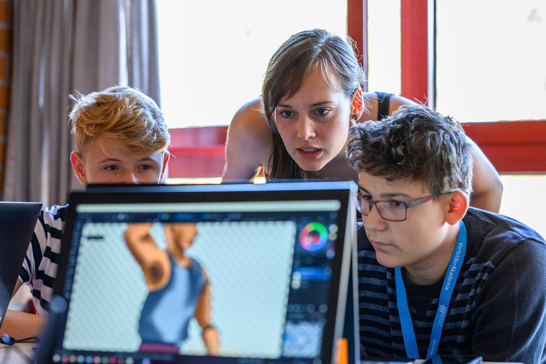Eine junge Frau und zwei Jungs schauen konzentriert auf einem Computer.
