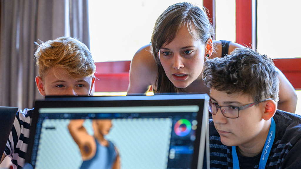 Eine junge Frau und zwei Jungs schauen konzentriert auf einem Computer.