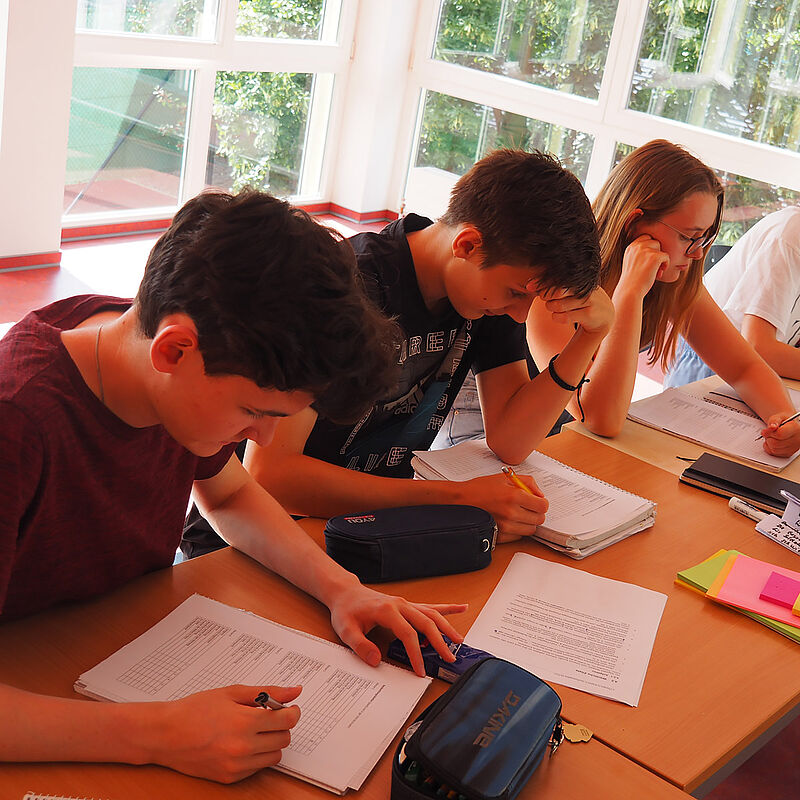 Drei Jugendliche sitzen an einem Tisch und Arbeiten auf Papier.